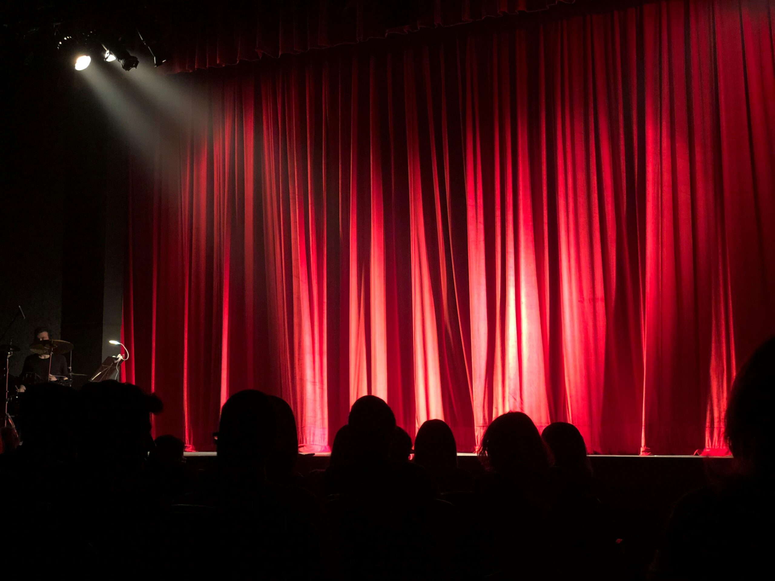 Picture of silhouette of people in a theater with a red drape int he background.